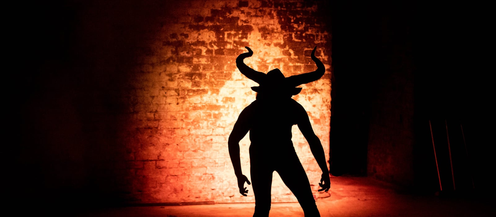Silhouette of the Minotaur against a brick wall lit in fiery orange at The Vaults