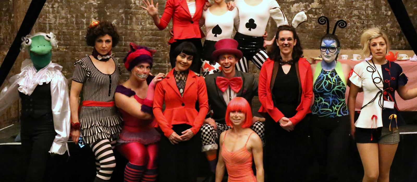 Full cast of Down the Rabbit Hole in Wonderland costumes, posed together beside the tea party table