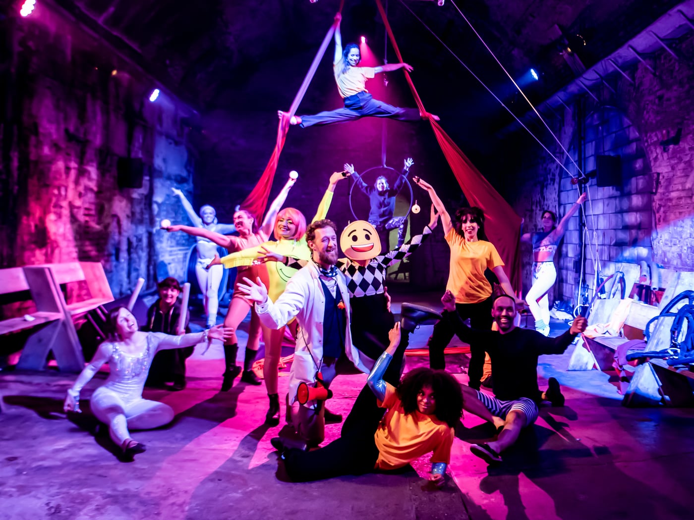 Full Happy Factory company pose across the vault floor with aerialists on silks and hoop above