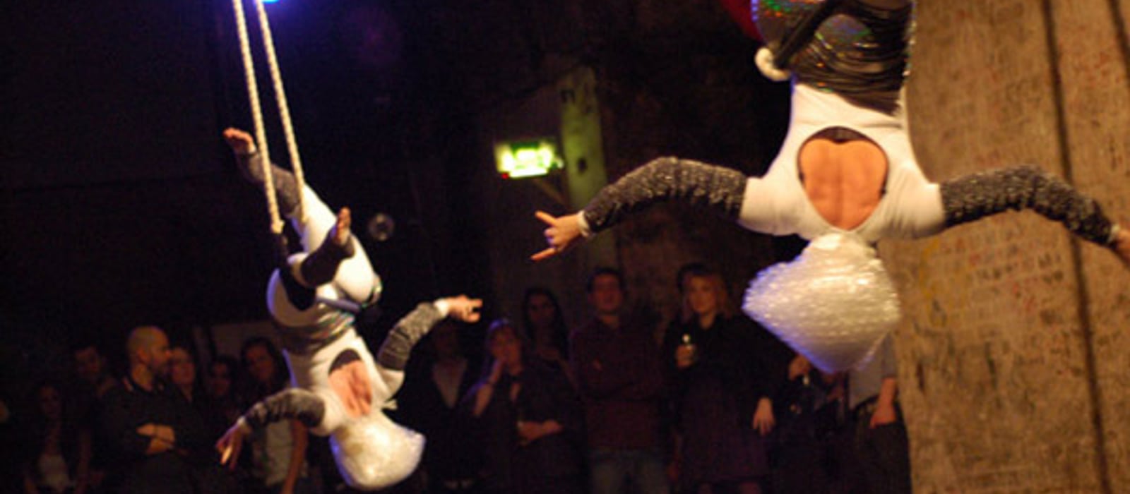 Two aerialists in bubble-wrap headpieces hang from ropes under the brick arches at Shunt, with the audience watching below